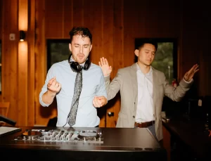 Two suited men posing in front of a DJ booth, exuding professionalism and style.