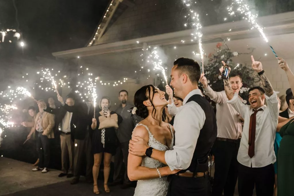 A newlywed couple surrounded by friends, capturing the moment with cellphone cameras as they are holding light stick